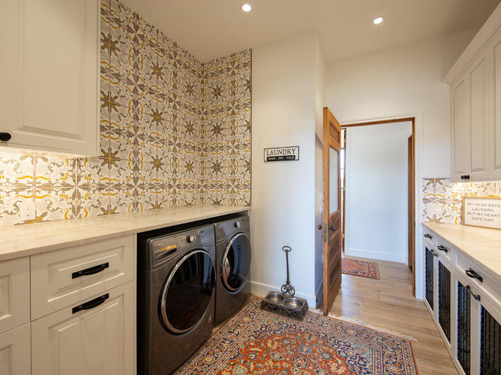 This is an example of a country galley dedicated laundry room in Austin with raised-panel cabinets, white cabinets, quartzite benchtops, white walls, medium hardwood floors, a side-by-side washer and dryer, beige floor and beige benchtop.