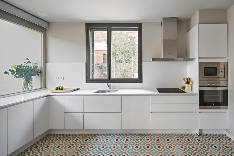 Contemporary l-shaped kitchen in Barcelona with an undermount sink, flat-panel cabinets, white cabinets, stainless steel appliances, multi-coloured floor and white benchtop.