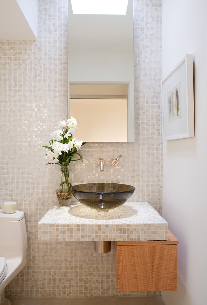 Powder room - contemporary beige tile and mosaic tile powder room idea in Los Angeles with light wood cabinets, a one-piece toilet, white walls, a vessel sink, tile countertops and flat-panel cabinets