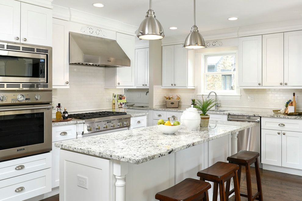 Photo of a traditional l-shaped kitchen in Chicago with an undermount sink, shaker cabinets, white cabinets, white splashback, subway tile splashback, stainless steel appliances, dark hardwood floors and with island.