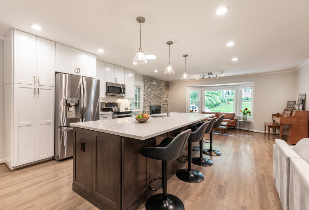 Design ideas for a mid-sized contemporary eat-in kitchen in DC Metro with an undermount sink, flat-panel cabinets, white cabinets, white splashback, stainless steel appliances, light hardwood floors, with island, brown floor and white benchtop.