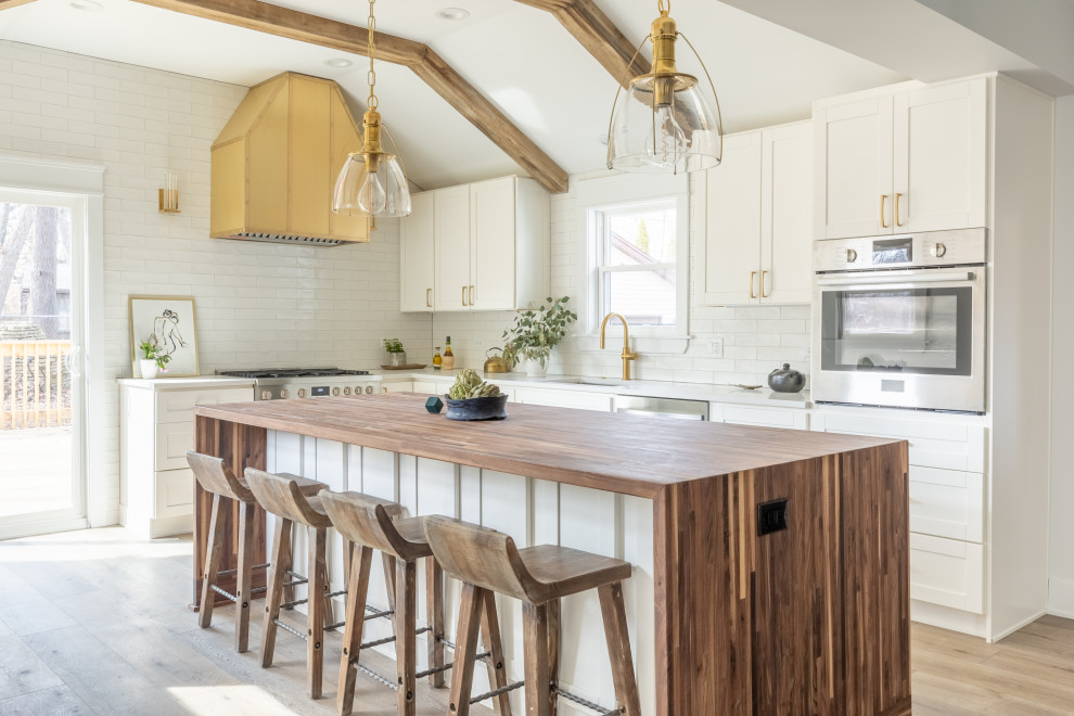 Inspiration for a transitional l-shaped kitchen in Other with an undermount sink, shaker cabinets, white cabinets, white splashback, subway tile splashback, stainless steel appliances, light hardwood floors, with island, beige floor, white benchtop, exposed beam and vaulted.