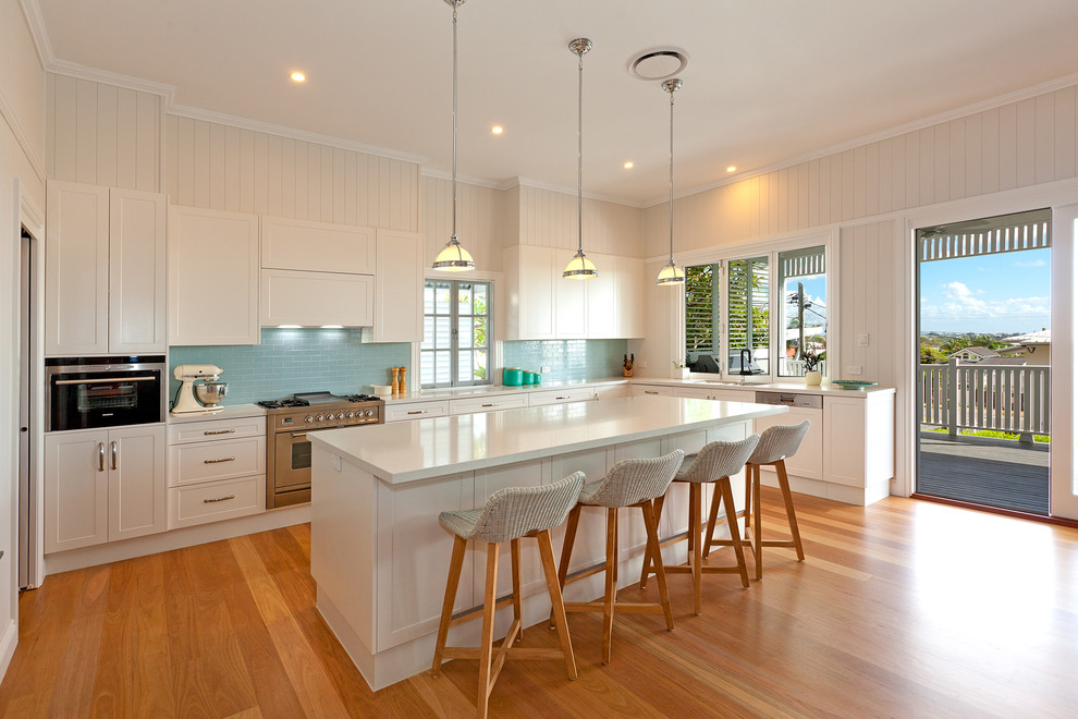 Photo of a large traditional l-shaped kitchen pantry in Brisbane with an undermount sink, shaker cabinets, white cabinets, quartz benchtops, blue splashback, ceramic splashback, stainless steel appliances, light hardwood floors and with island.