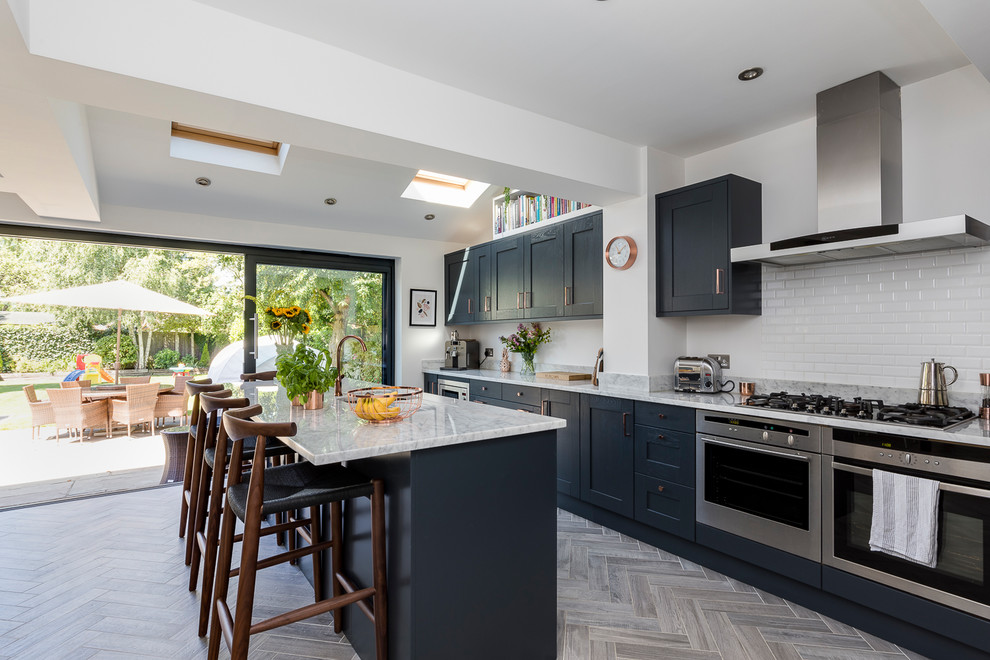 Mid-sized contemporary single-wall kitchen in London with recessed-panel cabinets, blue cabinets, marble benchtops, white splashback, subway tile splashback, stainless steel appliances and a peninsula.