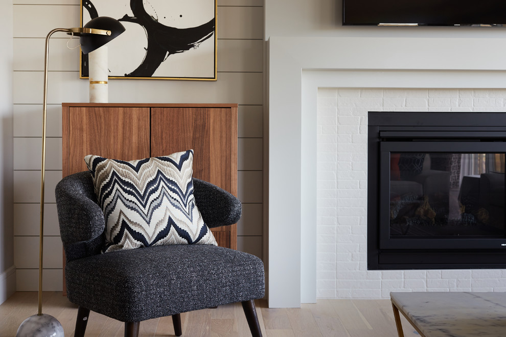 This is an example of a mid-sized transitional open concept living room in Edmonton with white walls, light hardwood floors, a standard fireplace, a brick fireplace surround and a wall-mounted tv.