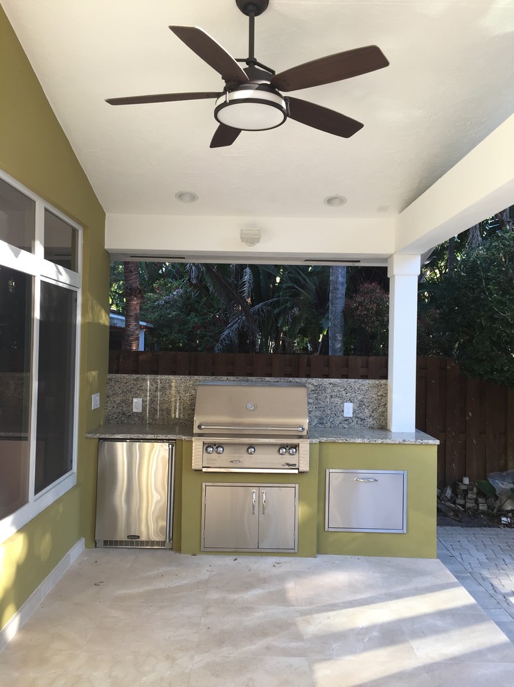 This is an example of a mid-sized backyard verandah in Miami with an outdoor kitchen, natural stone pavers and a roof extension.