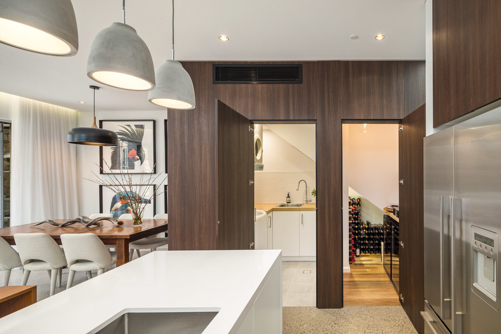 Mid-sized contemporary u-shaped dedicated laundry room in Sydney with a drop-in sink, recessed-panel cabinets, white cabinets, wood benchtops, white walls, porcelain floors and a stacked washer and dryer.