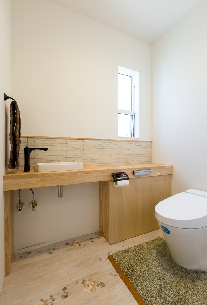 Scandinavian powder room in Other with white walls, light hardwood floors, a vessel sink, flat-panel cabinets, light wood cabinets, a wall-mount toilet, beige tile and wood benchtops.