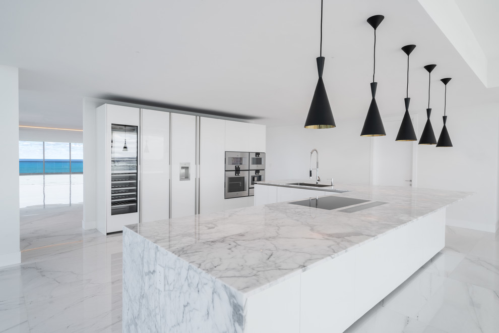 Design ideas for a large modern galley open plan kitchen in Miami with an undermount sink, flat-panel cabinets, white cabinets, marble benchtops, white appliances, marble floors, with island, white floor and white benchtop.