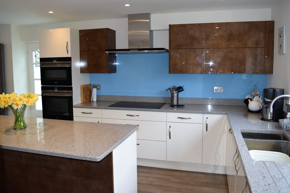 Photo of a mid-sized contemporary eat-in kitchen in Hampshire with white cabinets, quartz benchtops, blue splashback, glass sheet splashback, black appliances, vinyl floors and with island.