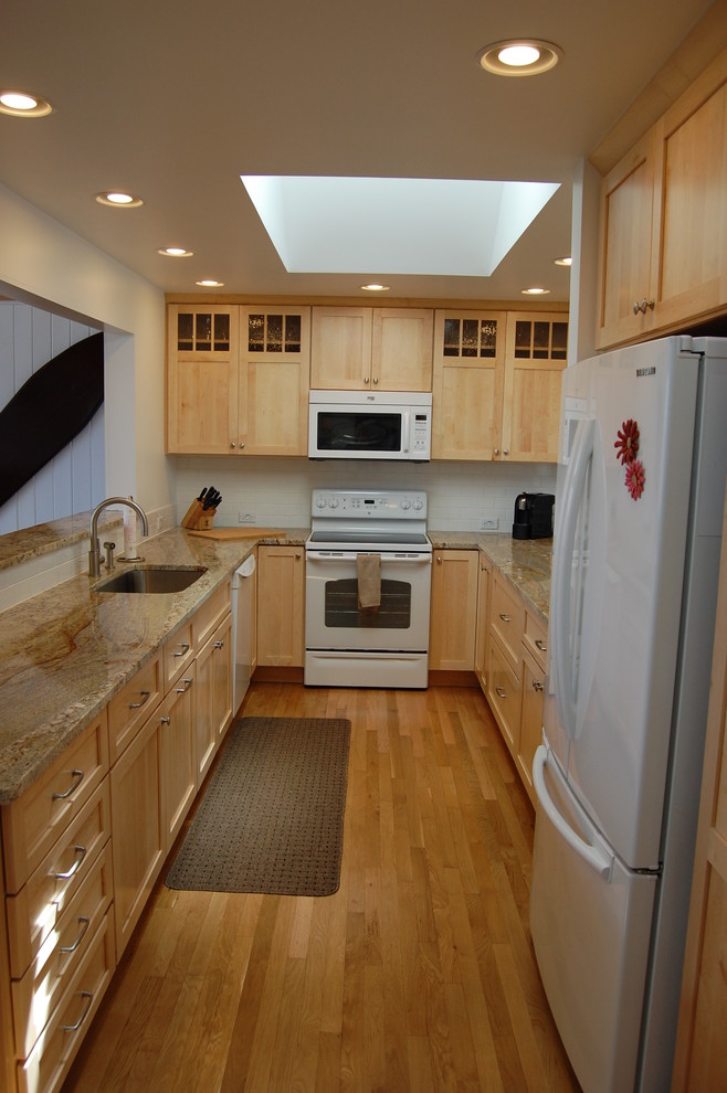 This is an example of a mid-sized arts and crafts galley separate kitchen in Burlington with an undermount sink, shaker cabinets, light wood cabinets, granite benchtops, white splashback, ceramic splashback, white appliances, medium hardwood floors and no island.