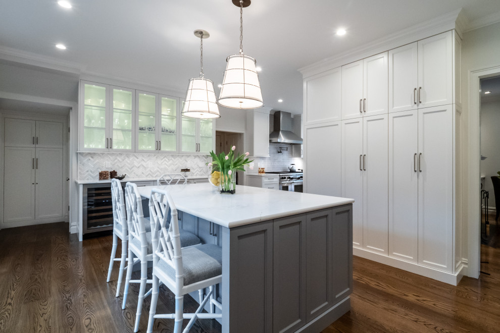 Klassische Wohnküche mit flächenbündigen Schrankfronten, Rückwand aus Marmor, Elektrogeräten mit Frontblende, braunem Holzboden, Kücheninsel und weißer Arbeitsplatte in Philadelphia