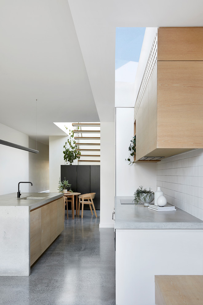 This is an example of a mid-sized contemporary galley open plan kitchen in Melbourne with a double-bowl sink, light wood cabinets, concrete benchtops, white splashback, ceramic splashback, stainless steel appliances, concrete floors, with island, grey floor and grey benchtop.