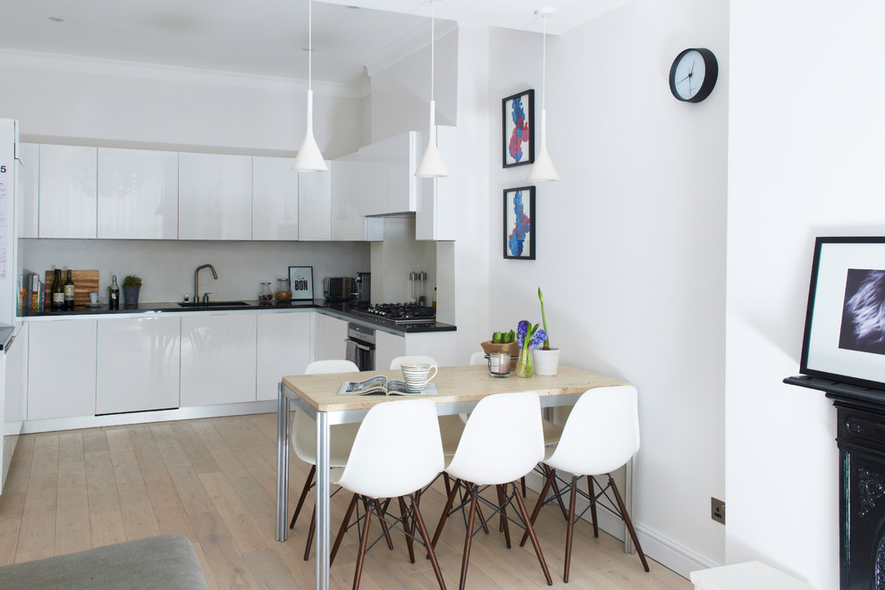 This is an example of a contemporary open plan kitchen in London with flat-panel cabinets, white cabinets, grey splashback, light hardwood floors and no island.