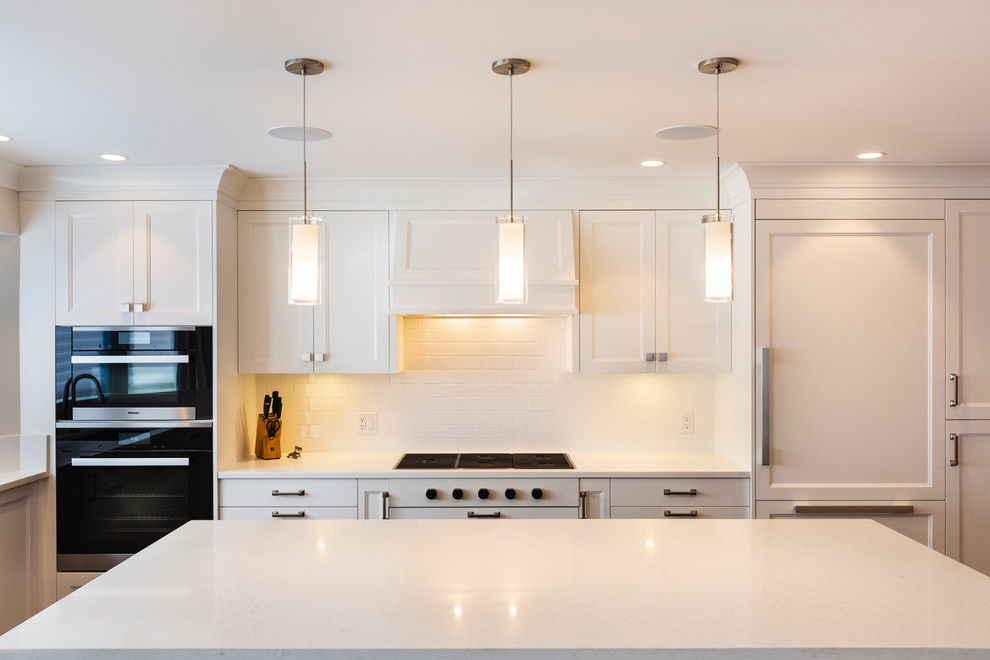 Large transitional l-shaped medium tone wood floor and brown floor open concept kitchen photo in Vancouver with an undermount sink, recessed-panel cabinets, white cabinets, quartz countertops, white backsplash, ceramic backsplash, paneled appliances, an island and white countertops