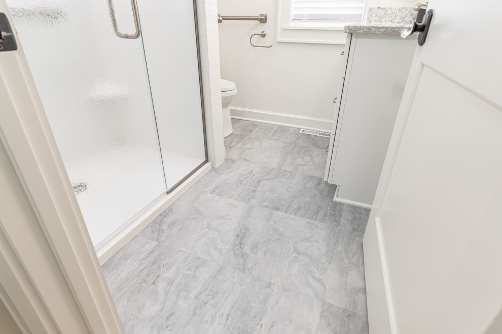 Mid-sized elegant wood-look tile floor, gray floor and single-sink corner shower photo in Milwaukee with shaker cabinets, white cabinets, a one-piece toilet, beige walls, an undermount sink, quartz countertops, a hinged shower door, multicolored countertops, a niche and a built-in vanity