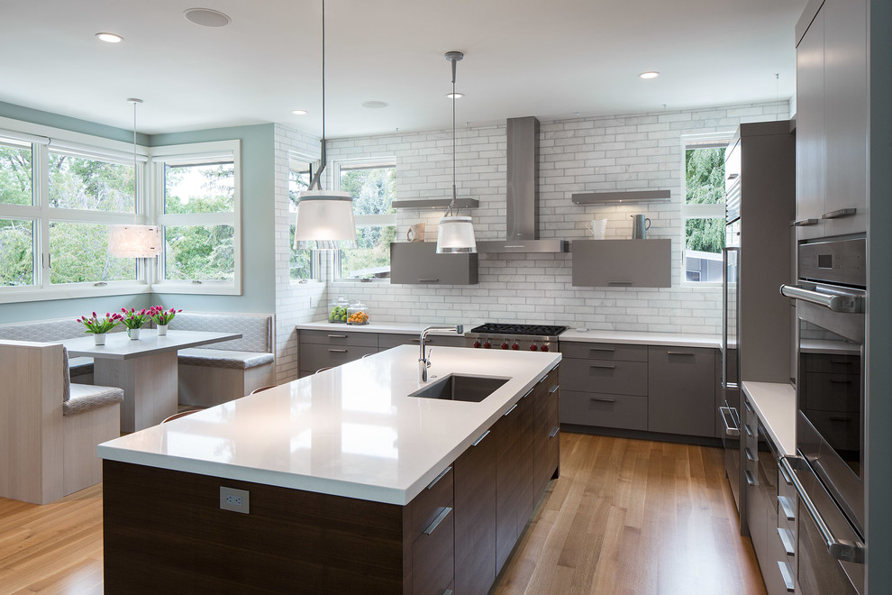 Contemporary eat-in kitchen in New York with an undermount sink, flat-panel cabinets, grey cabinets, white splashback, stainless steel appliances, light hardwood floors and with island.