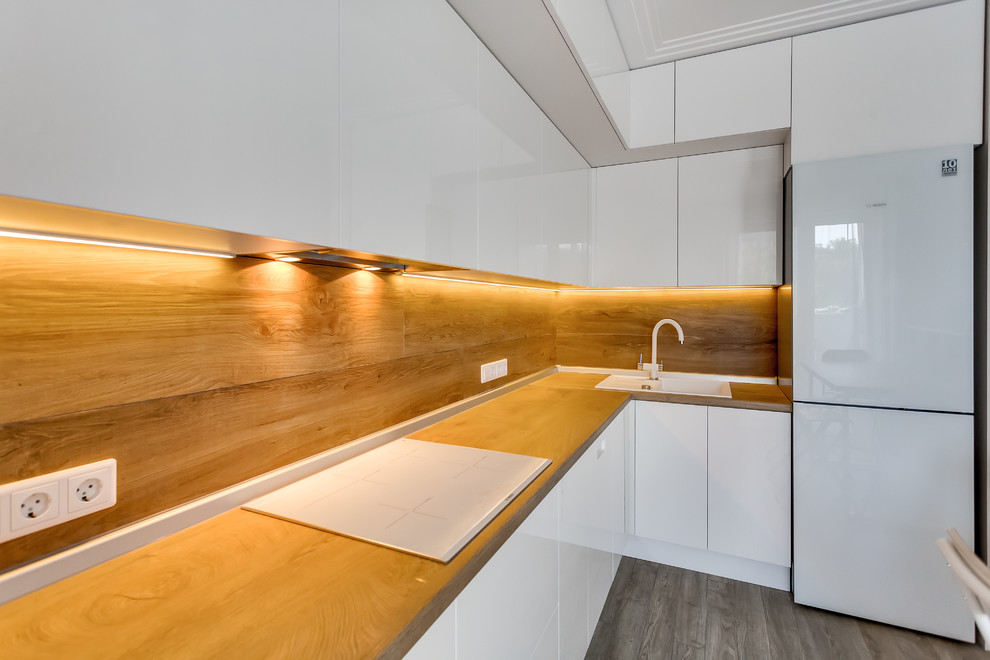 Photo of a mid-sized contemporary l-shaped open plan kitchen in Other with a drop-in sink, flat-panel cabinets, white cabinets, wood benchtops, porcelain splashback, white appliances, with island and grey floor.