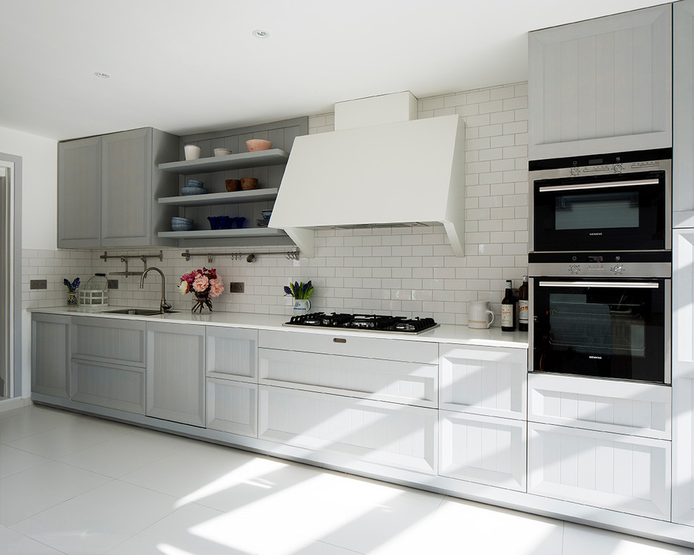 Mid-sized scandinavian single-wall eat-in kitchen in London with a single-bowl sink, raised-panel cabinets, grey cabinets, solid surface benchtops, white splashback, ceramic splashback, black appliances, porcelain floors, no island, white floor and white benchtop.