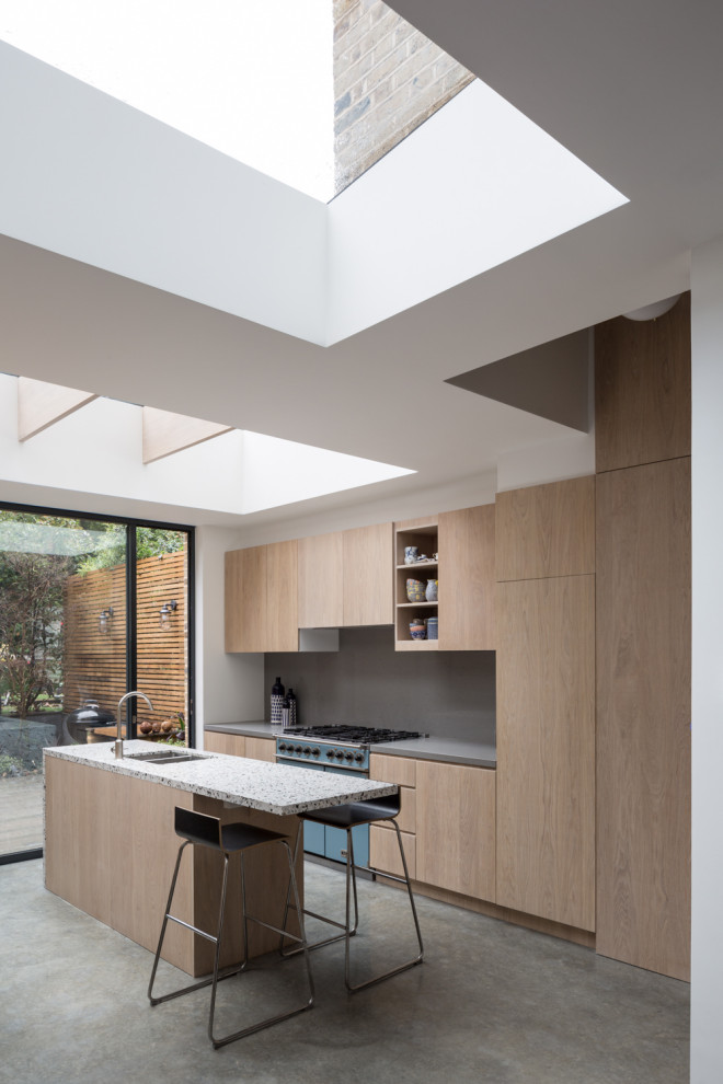 Inspiration for a mid-sized modern single-wall eat-in kitchen in Essex with an undermount sink, flat-panel cabinets, medium wood cabinets, terrazzo benchtops, grey splashback, limestone splashback, coloured appliances, concrete floors, with island, grey floor and multi-coloured benchtop.