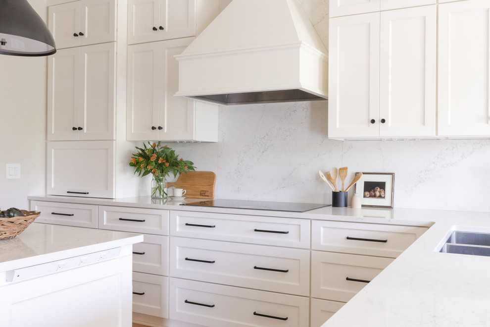 Inspiration for a large transitional light wood floor eat-in kitchen remodel with an undermount sink, shaker cabinets, white cabinets, quartz countertops, white backsplash, quartz backsplash, stainless steel appliances, an island and white countertops