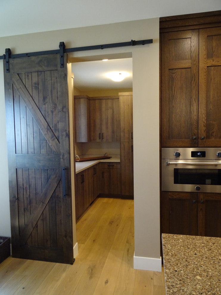 Example of a large transitional l-shaped light wood floor and brown floor kitchen pantry design with shaker cabinets, medium tone wood cabinets, granite countertops, an island and white countertops