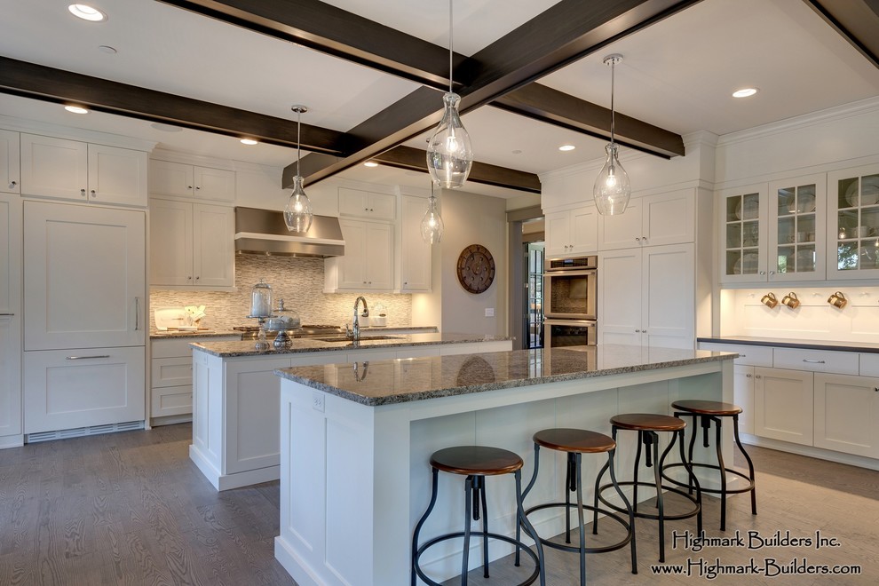 This is an example of an expansive traditional l-shaped open plan kitchen in Minneapolis with a double-bowl sink, shaker cabinets, white cabinets, granite benchtops, beige splashback, mosaic tile splashback, panelled appliances, light hardwood floors and multiple islands.