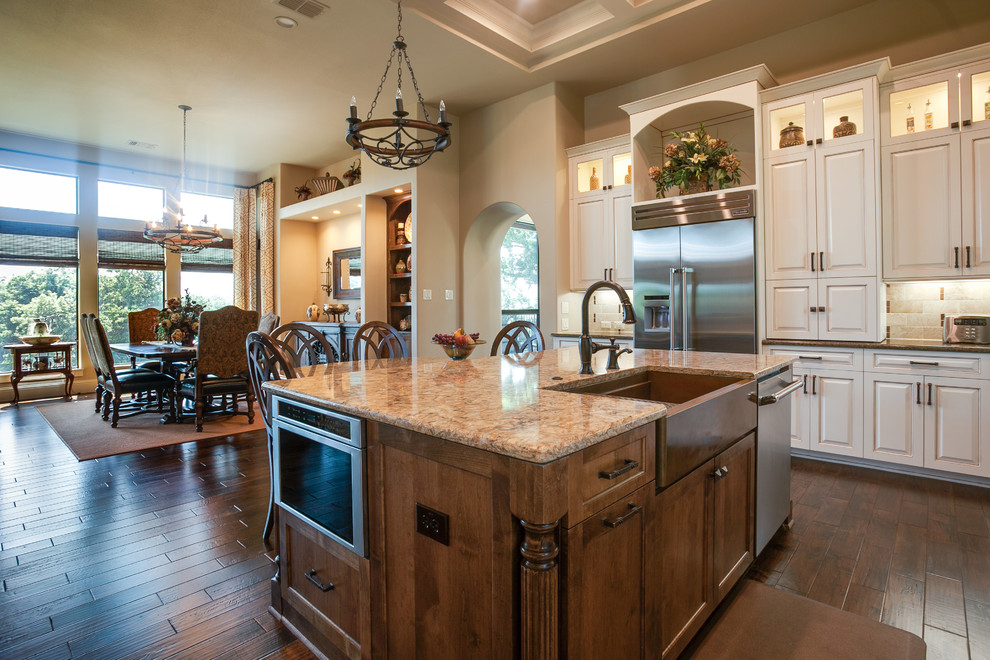 Design ideas for an expansive traditional l-shaped eat-in kitchen in Dallas with a farmhouse sink, louvered cabinets, granite benchtops, beige splashback, ceramic splashback, stainless steel appliances, dark hardwood floors and multiple islands.
