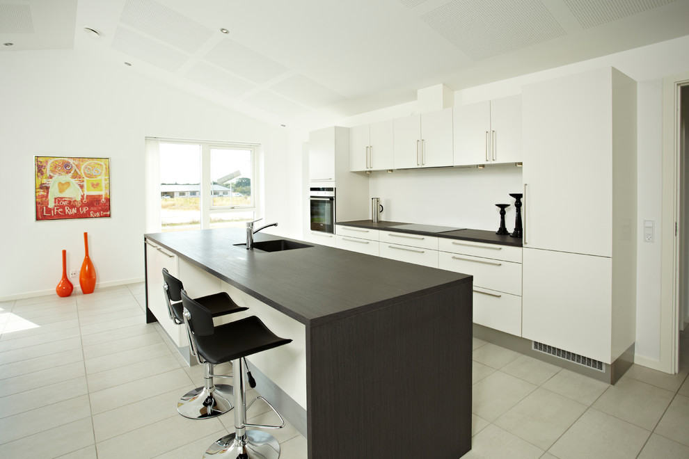 This is an example of a large contemporary galley open plan kitchen in Aarhus with an integrated sink, flat-panel cabinets, white cabinets, wood benchtops, stainless steel appliances and with island.