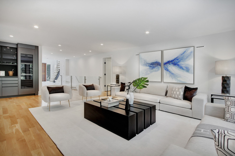 This is an example of a medium sized contemporary open plan living room in New York with a home bar, white walls, light hardwood flooring and a hanging fireplace.