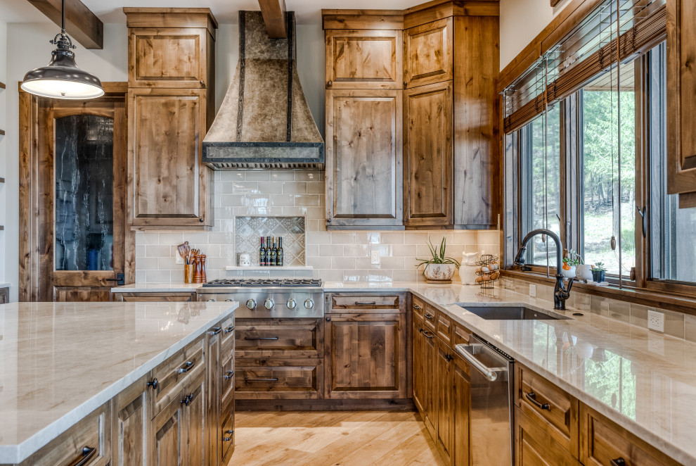 Inspiration for a rustic l-shaped light wood floor and beige floor kitchen remodel with an undermount sink, raised-panel cabinets, dark wood cabinets, gray backsplash, subway tile backsplash, stainless steel appliances, an island and gray countertops