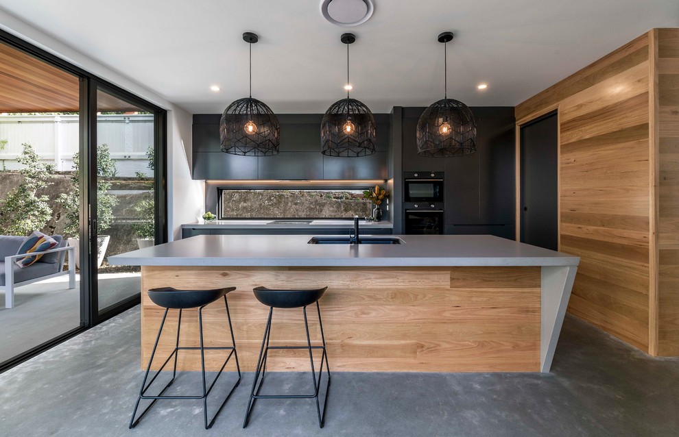 Contemporary galley kitchen in Brisbane with an undermount sink, flat-panel cabinets, black cabinets, concrete benchtops, window splashback, black appliances, concrete floors, with island, grey floor and grey benchtop.
