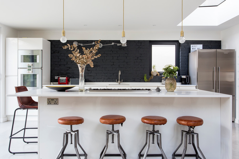 Mid-sized contemporary single-wall kitchen in London with an undermount sink, flat-panel cabinets, black splashback, brick splashback, stainless steel appliances, concrete floors, with island, grey floor and white benchtop.