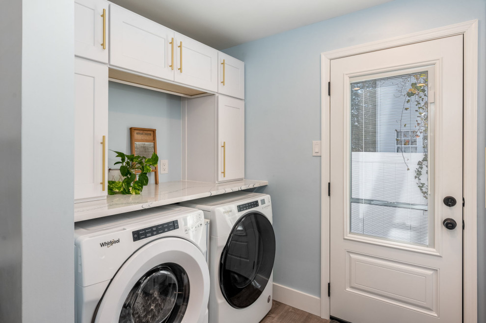 Foto på en liten flerfärgade u-formad tvättstuga enbart för tvätt, med luckor med infälld panel, vita skåp, bänkskiva i kvarts, vitt stänkskydd, blå väggar och en tvättmaskin och torktumlare bredvid varandra