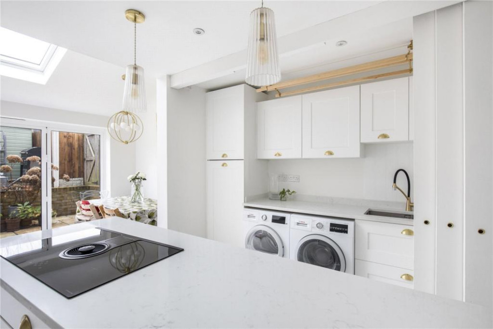 Medium sized contemporary galley kitchen/diner in London with shaker cabinets, white cabinets, composite countertops, porcelain flooring, an island, white floors, white worktops and a feature wall.