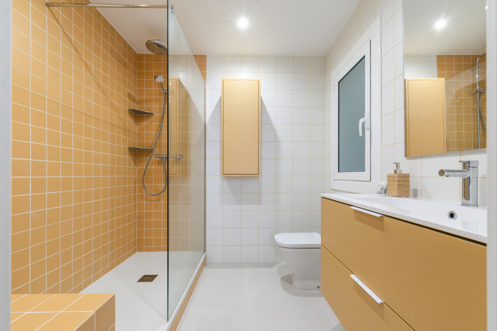 Inredning av ett modernt stort vit vitt en-suite badrum, med släta luckor, gula skåp, en öppen dusch, en toalettstol med hel cisternkåpa, gul kakel, keramikplattor, vita väggar, klinkergolv i keramik, ett integrerad handfat, bänkskiva i akrylsten och grått golv