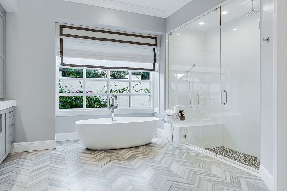 Mid-sized transitional master bathroom in Miami with shaker cabinets, grey cabinets, a freestanding tub, an alcove shower, grey walls, porcelain floors, an undermount sink, solid surface benchtops, grey floor, a hinged shower door and white benchtops.