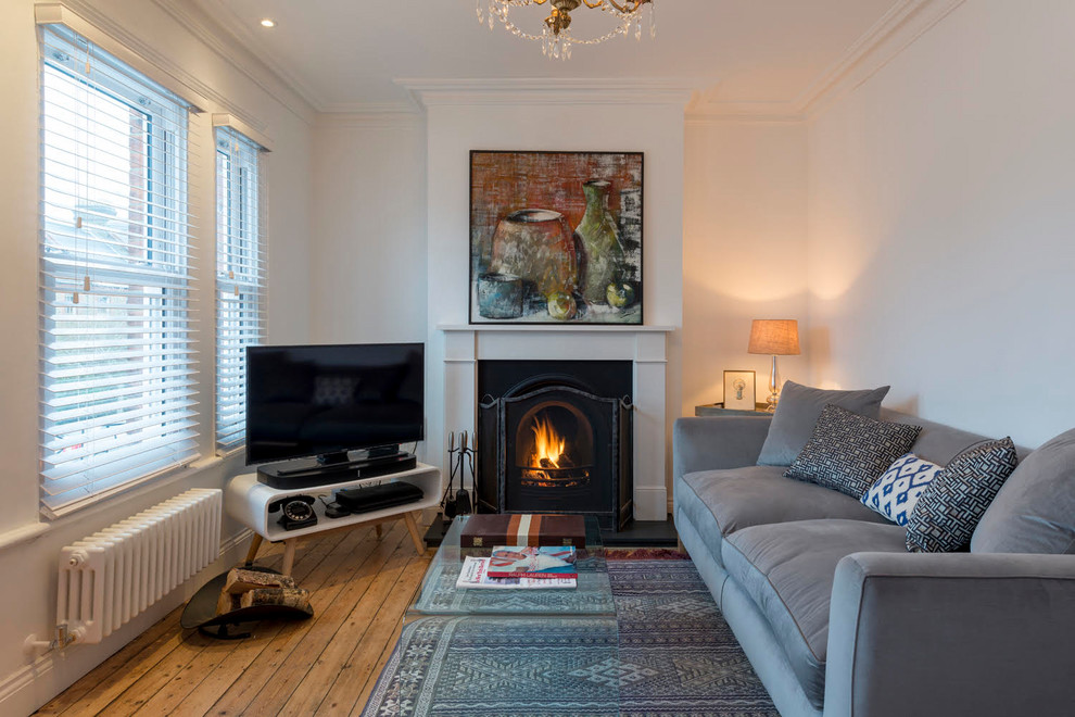 This is an example of a traditional formal enclosed living room in London with white walls, medium hardwood floors, a standard fireplace, a freestanding tv and brown floor.