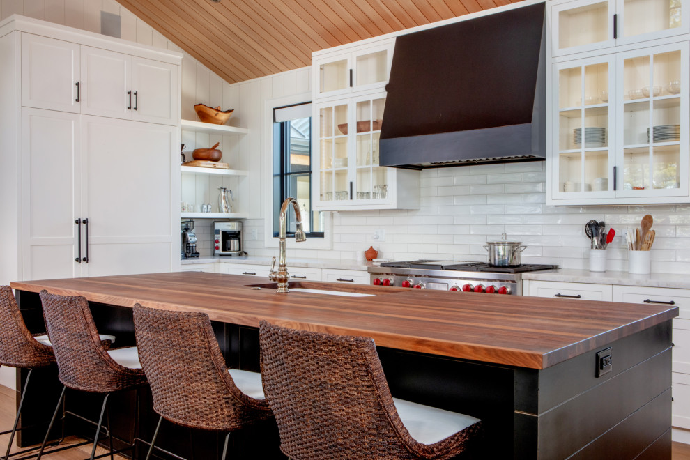 Klassisk inredning av ett mellanstort brun brunt kök, med en undermonterad diskho, skåp i shakerstil, vita skåp, träbänkskiva, vitt stänkskydd, stänkskydd i tunnelbanekakel, rostfria vitvaror, mellanmörkt trägolv, en köksö och brunt golv