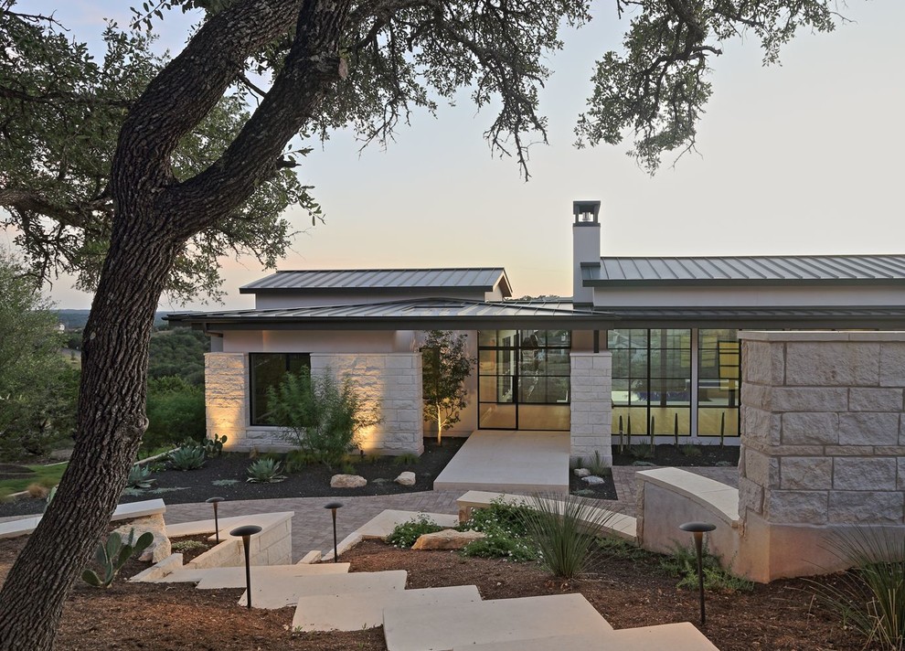 Photo of a large contemporary two-storey white house exterior in Austin with stone veneer, a gable roof and a metal roof.