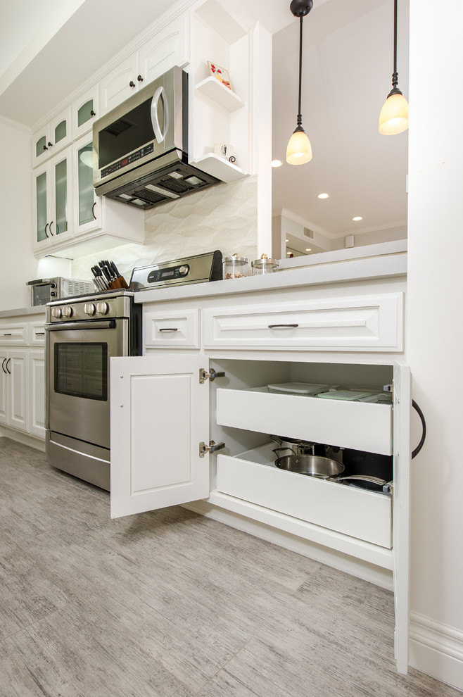 Inspiration for a small traditional galley separate kitchen in Los Angeles with an undermount sink, glass-front cabinets, white cabinets, quartz benchtops, beige splashback, ceramic splashback, stainless steel appliances and porcelain floors.