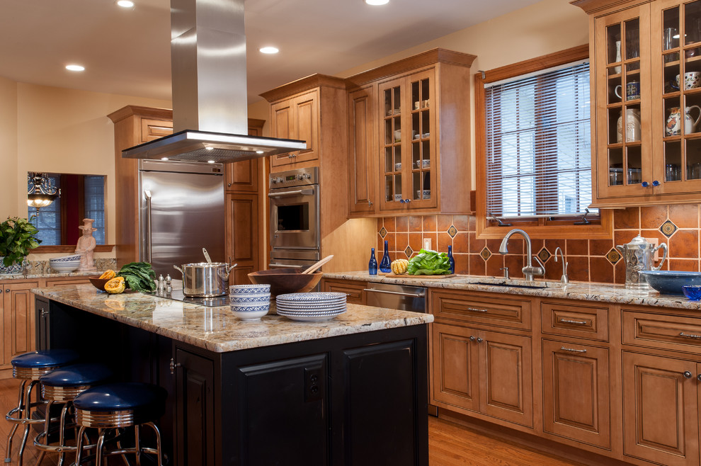 Photo of a traditional l-shaped kitchen in St Louis with an undermount sink, raised-panel cabinets, medium wood cabinets, granite benchtops, brown splashback and stainless steel appliances.