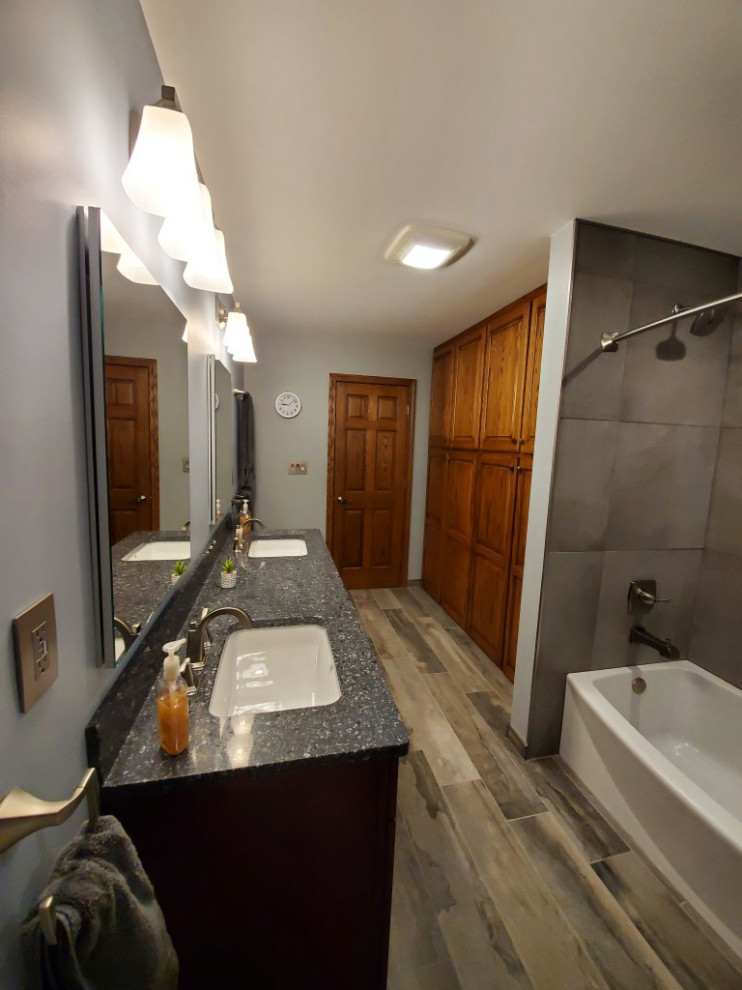 Example of a mid-sized transitional master gray tile and porcelain tile porcelain tile, brown floor and double-sink alcove bathtub design with recessed-panel cabinets, dark wood cabinets, blue walls, an undermount sink, quartz countertops, blue countertops and a niche