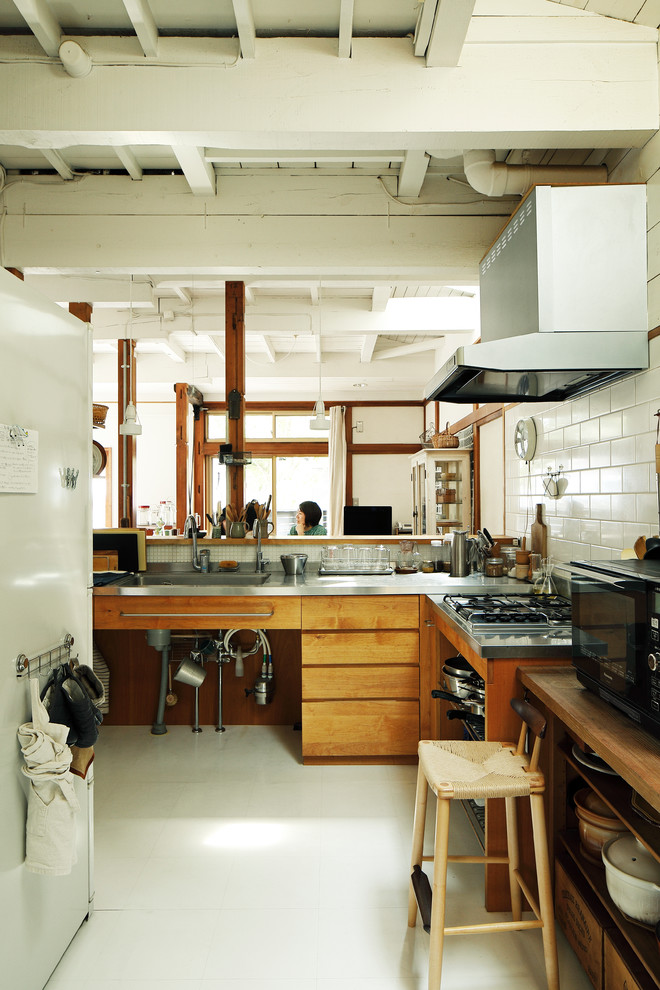 This is an example of an asian l-shaped open plan kitchen in Tokyo Suburbs with a single-bowl sink, flat-panel cabinets, medium wood cabinets, stainless steel benchtops, white splashback, a peninsula and white floor.