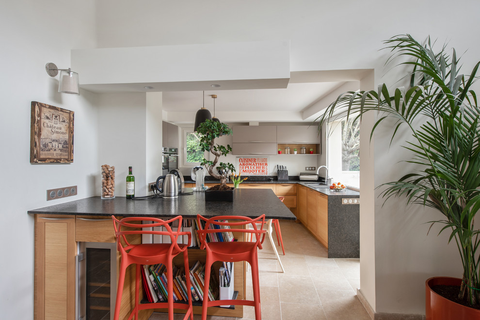 This is an example of a large contemporary u-shaped kitchen in Marseille with an undermount sink, flat-panel cabinets, medium wood cabinets, white splashback, window splashback, stainless steel appliances, beige floor and black benchtop.