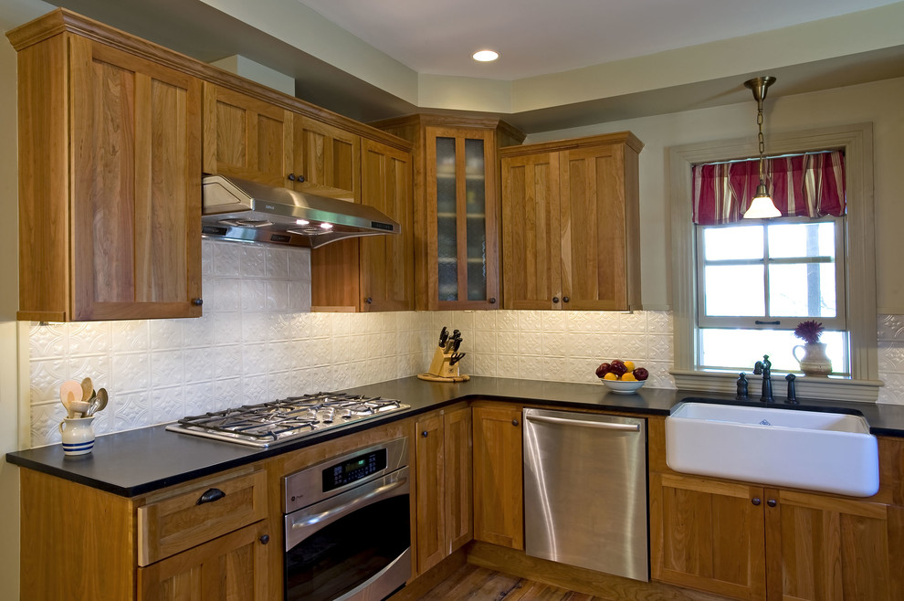 Design ideas for a mid-sized traditional l-shaped kitchen in Philadelphia with stainless steel appliances, a farmhouse sink, flat-panel cabinets, medium wood cabinets, soapstone benchtops, white splashback, metal splashback, light hardwood floors and no island.