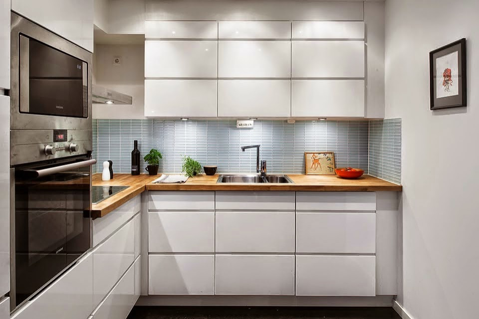 Inspiration for a small tropical l-shaped separate kitchen in Madrid with a farmhouse sink, flat-panel cabinets, white cabinets, wood benchtops, stainless steel appliances, ceramic floors, no island, black floor and brown benchtop.