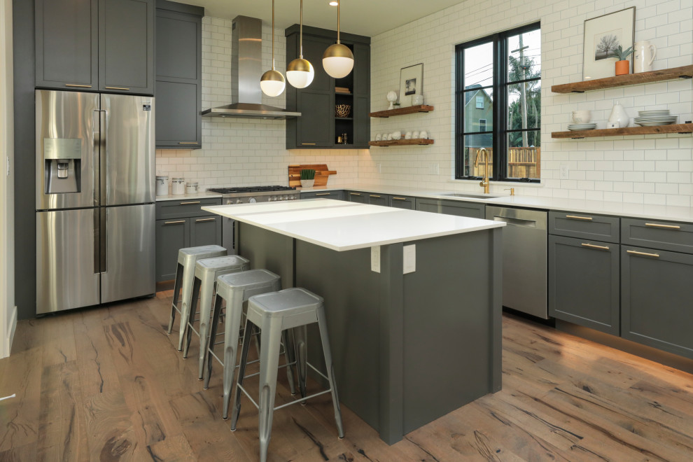 Mid-sized transitional l-shaped eat-in kitchen in San Francisco with a drop-in sink, recessed-panel cabinets, grey cabinets, quartz benchtops, white splashback, subway tile splashback, stainless steel appliances, light hardwood floors, with island, multi-coloured floor, white benchtop and recessed.