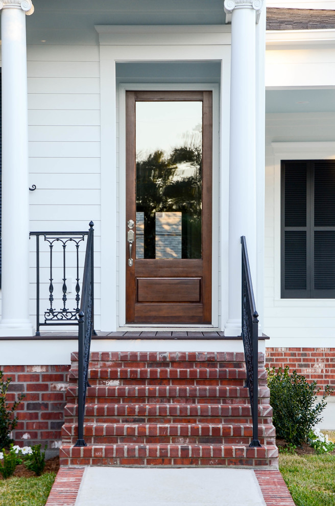 This is an example of a mid-sized traditional front door in New Orleans with white walls, a single front door and a medium wood front door.
