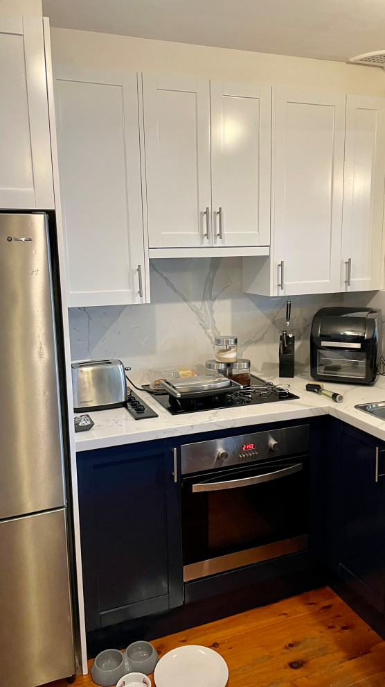 Design ideas for a mid-sized contemporary u-shaped kitchen pantry in Sydney with a double-bowl sink, shaker cabinets, blue cabinets, quartz benchtops, white splashback, engineered quartz splashback, stainless steel appliances, light hardwood floors, no island, yellow floor and white benchtop.